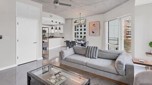 Een moderne woonkamer met een glazen salontafel, een grijze bank en een plafondventilator.