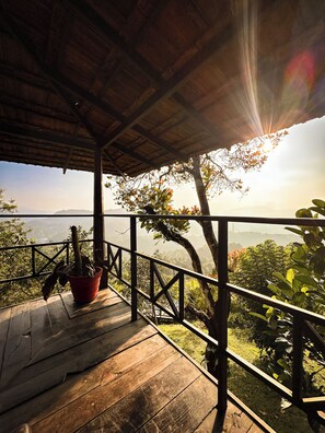 Terraza de madera con barandilla, una maceta y vistas a un paisaje con árboles y colinas.