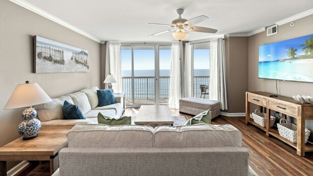 A living room with a sofa, a coffee table, a TV, and a balcony with a view of the ocean. - Sunrise Pointe 9E-Oceanfront 3BR-Pool, Hot Tub (North Myrtle Beach)