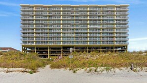 A multi-story hotel with balconies, located on a sandy beachfront with sparse vegetation. - Sunrise Pointe 9E-Oceanfront 3BR-Pool, Hot Tub (North Myrtle Beach)