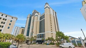 A multi-story hotel with a central atrium, palm trees, and a street in front. - Breakers 372-Oceanfront 1BR - Close to Boardwalk (Myrtle Beach)