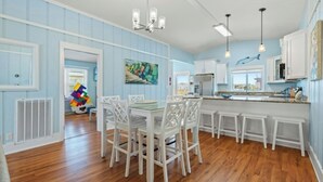 A spacious kitchen with white cabinetry, a central island, and a dining area with white chairs. - The Reagan- 4BR Channel House-Hot Tub (North Myrtle Beach)