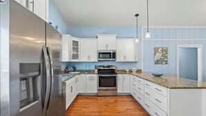 A modern kitchen with white cabinets, stainless steel appliances, and a wooden floor. - The Reagan- 4BR Channel House-Hot Tub (North Myrtle Beach)