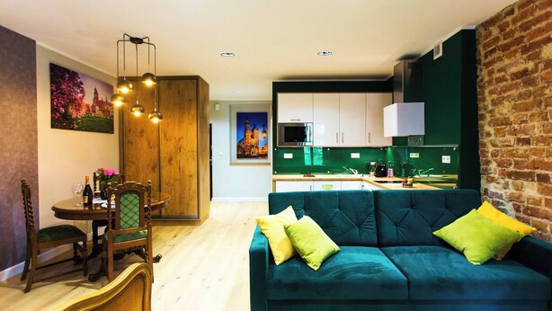Una sala de estar moderna con un sofá verde, una mesa de comedor de madera y una cocina al fondo.