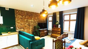 Un salón moderno con pared de ladrillo, un sofá color turquesa, un aparador de madera y una cama con toallas enrolladas.