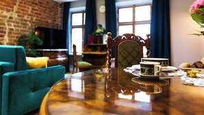 Un cuarto acogedor con pared de ladrillo, una mesa redonda de madera con juego de té, un sillón azul y un sofá verde.