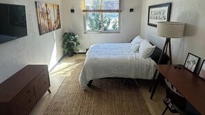 Een slaapkamer met een bed, een bureau, een lamp en een raam met jaloezieën.