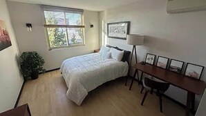 Een slaapkamer met een bed, een bureau, een stoel, een raam en een plant.