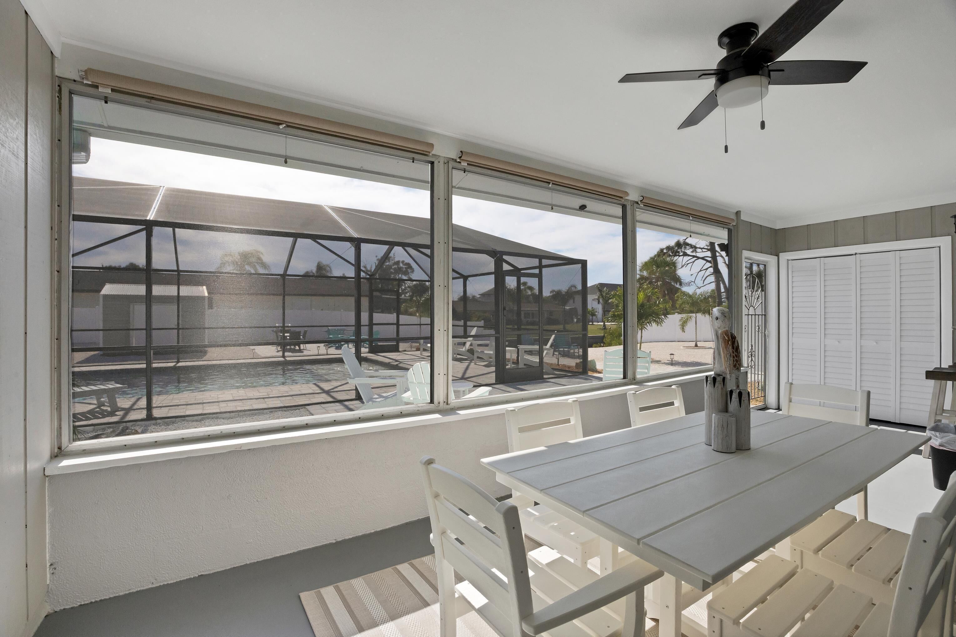 A room with a large window overlooking a pool area, a ceiling fan, and a table with chairs.