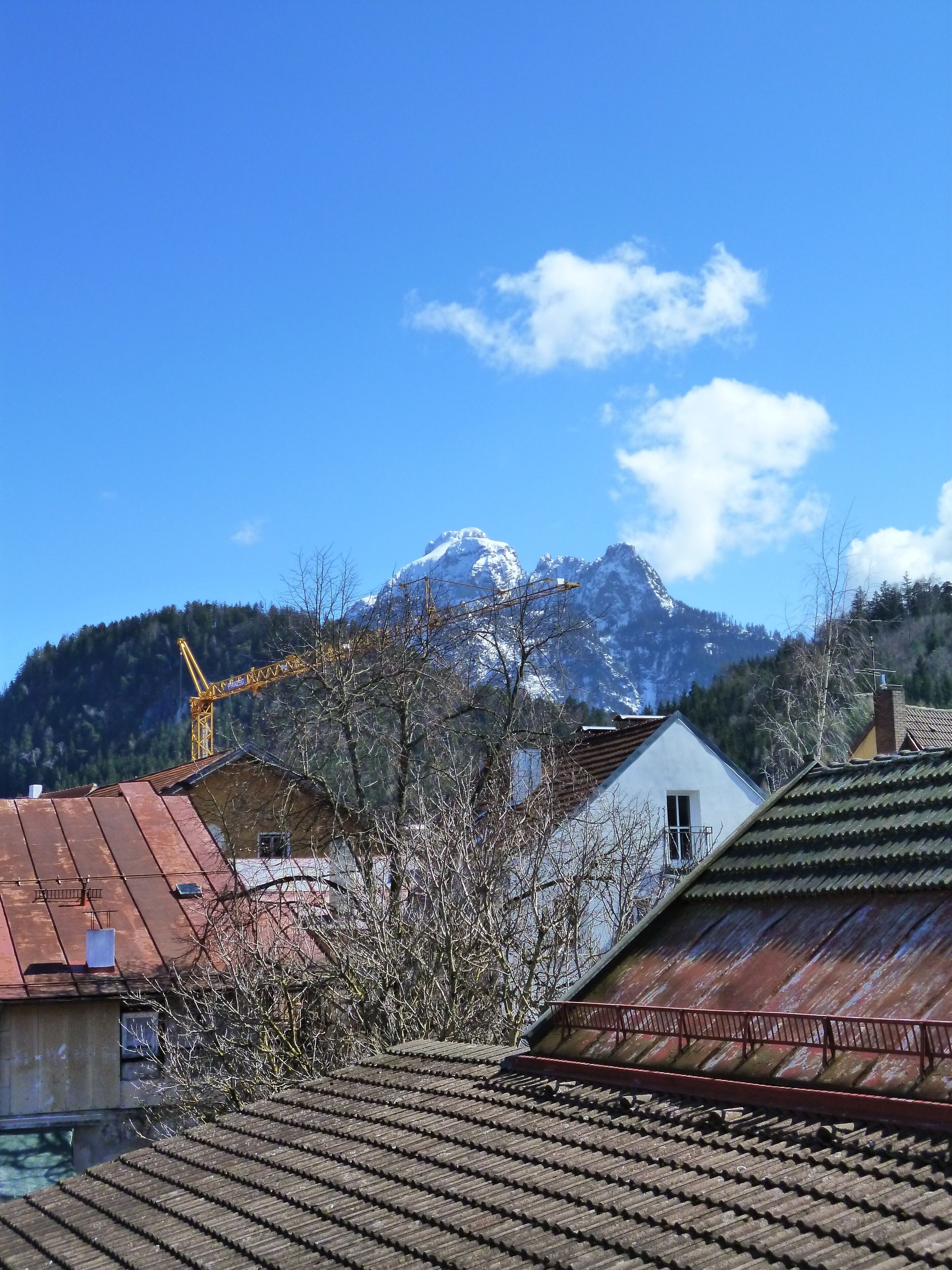 Eine Berglandschaft mit schneebedecktem Gipfel, Häusern mit roten Dächern und einem Baukran im Hintergrund.