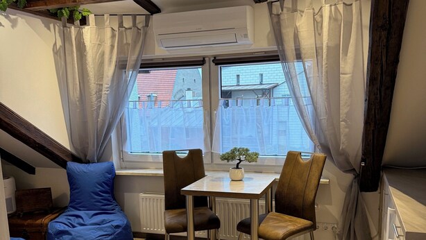 A cozy room with a wooden ceiling, a dining table with chairs, a blue bean bag, and a small potted plant. - Lucky Home Relax Apartment (Füssen)
