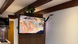 A modern room with a flat-screen TV mounted on a wooden wall, a kitchenette with a Bosch microwave, and a bed with striped bedding. - Lucky Home Relax Apartment (Füssen)