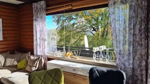 A cozy cabin-style room with wooden walls, a cushioned sofa, a dining table with glassware, and a view of trees and a bird outside. - Near Pullmann City - small house in the middle of nature... Vacation for the whole year... (Windorf)