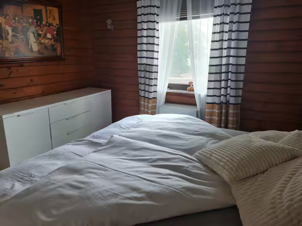 Une chambre à coucher avec un lit, une fenêtre avec des rideaux à rayures, un radiateur et un tableau accroché au mur.