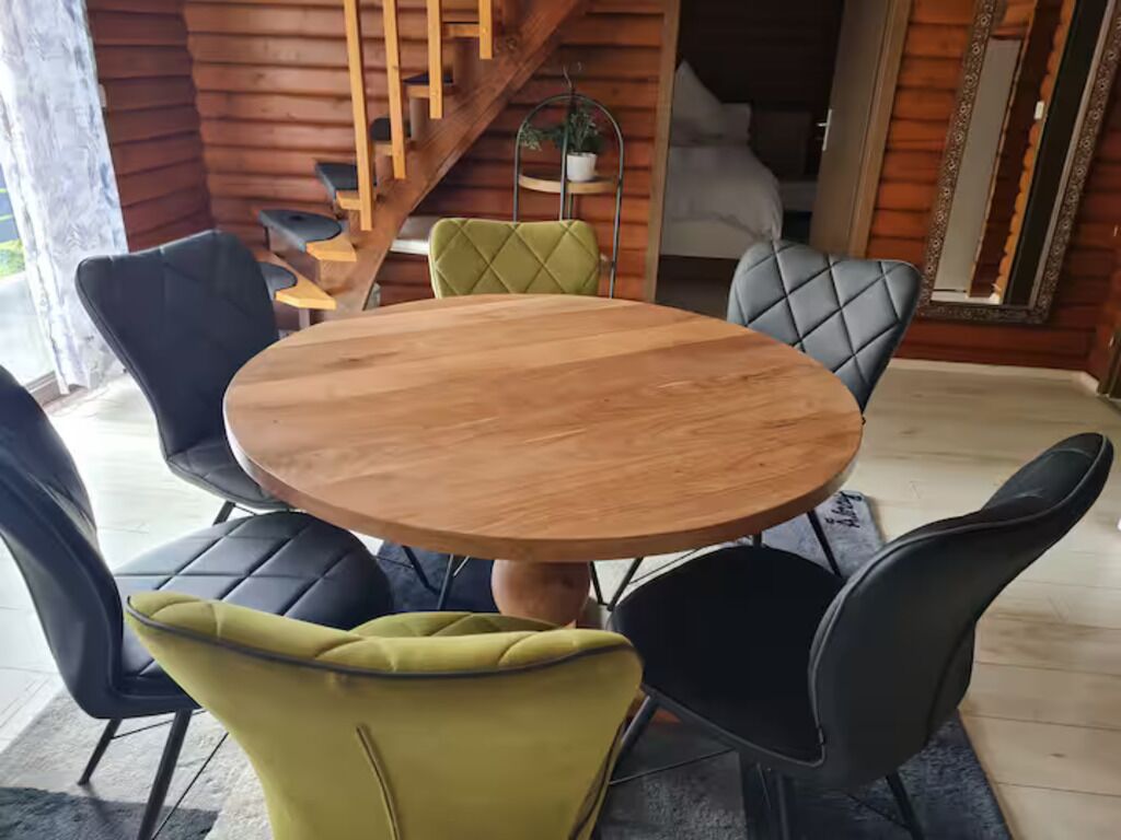 Una mesa de madera para comer rodeada de cuatro sillas, con una escalera y un espejo al fondo.