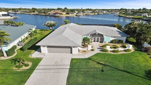 A residential property with a large garage, a well-maintained lawn, and a view of a lake with docks. - Amazing - 4 Bed Billiard Table Luxury Canal Pool (Cape Coral)