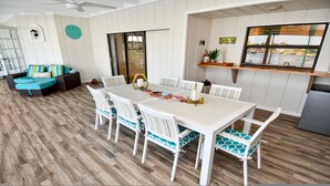 A dining area with a white table and chairs, a wooden floor, and a view of the outdoors through a window. - Amazing - 4 Bed Billiard Table Luxury Canal Pool (Cape Coral)