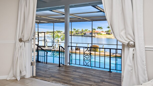 A view from a balcony with a pool, featuring a clear view of a body of water and palm trees in the background. - Amazing - 4 Bed Billiard Table Luxury Canal Pool (Cape Coral)