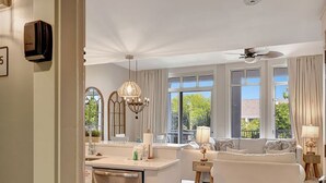 A spacious living area with a kitchen, large windows, and a ceiling fan.