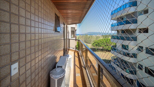 A balcony with a view of a modern building, a tiled wall, and a metal fence. - Cf05 Prédio beira mar Apto 3 quartos (Cabo Frio)