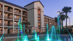 Un hotel con varios balcones, un patio central con fuentes y palmeras.