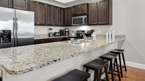 Una cocina con alacenas de madera oscura, electrodomésticos de acero inoxidable, encimeras de granito y taburetes de bar.