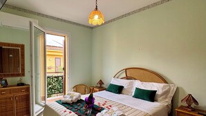 Une chambre bien rangée, avec un lit, des tables de chevet, une armoire et un balcon visible à travers la porte.