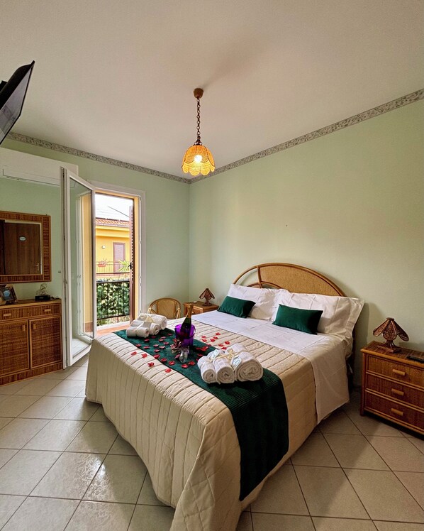 A neatly arranged bedroom with a bed, bedside tables, a wardrobe, and a balcony visible through the door.