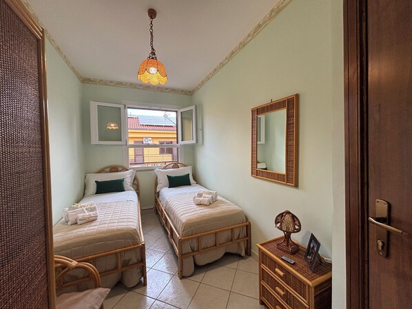 Una habitación con dos camas, una ventana, un espejo y una lámpara colgante.