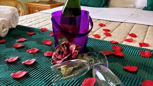Un lit recouvert d’une couverture verte et blanche, un seau violet, une bouteille de champagne et des pétales de roses rouges éparpillés sur le lit.