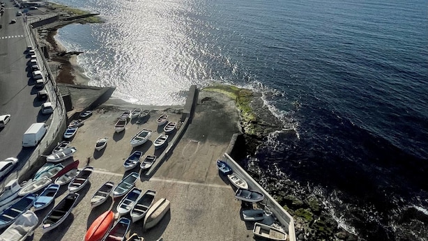 Un parking situé en bord de mer, avec des bateaux et une vue dégagée sur la mer et les montagnes lointaines.
