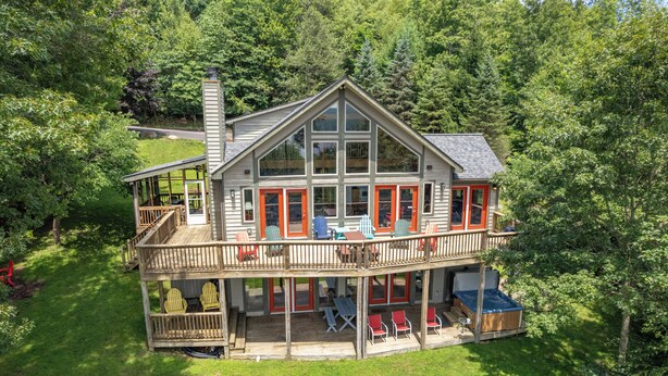 A two-story wooden house with a balcony, outdoor seating, and a hot tub. - Chic Dog Friendly Chalet w/ Fire Pit & Hot Tub (McHenry)
