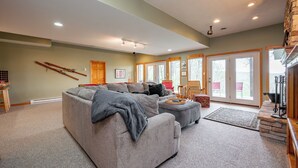 A spacious living room with a large sectional sofa, a fireplace, and a view through the glass doors. - Chic Dog Friendly Chalet w/ Fire Pit & Hot Tub (McHenry)