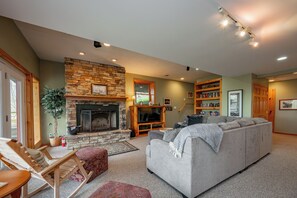 A cozy living room with a stone fireplace, a grey sofa, a wooden rocking chair, and a bookshelf. - Chic Dog Friendly Chalet w/ Fire Pit & Hot Tub (McHenry)