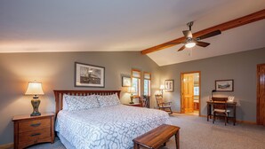 A bedroom with a large bed, a wooden nightstand with a lamp, a ceiling fan, and a desk with a chair. - Chic Dog Friendly Chalet w/ Fire Pit & Hot Tub (McHenry)