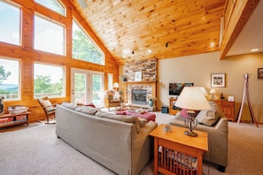 A cozy living room with a fireplace, large windows, and a stone accent wall.