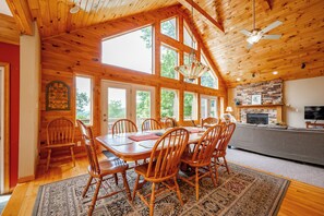 A wooden interior with a dining area, kitchen, and large windows.