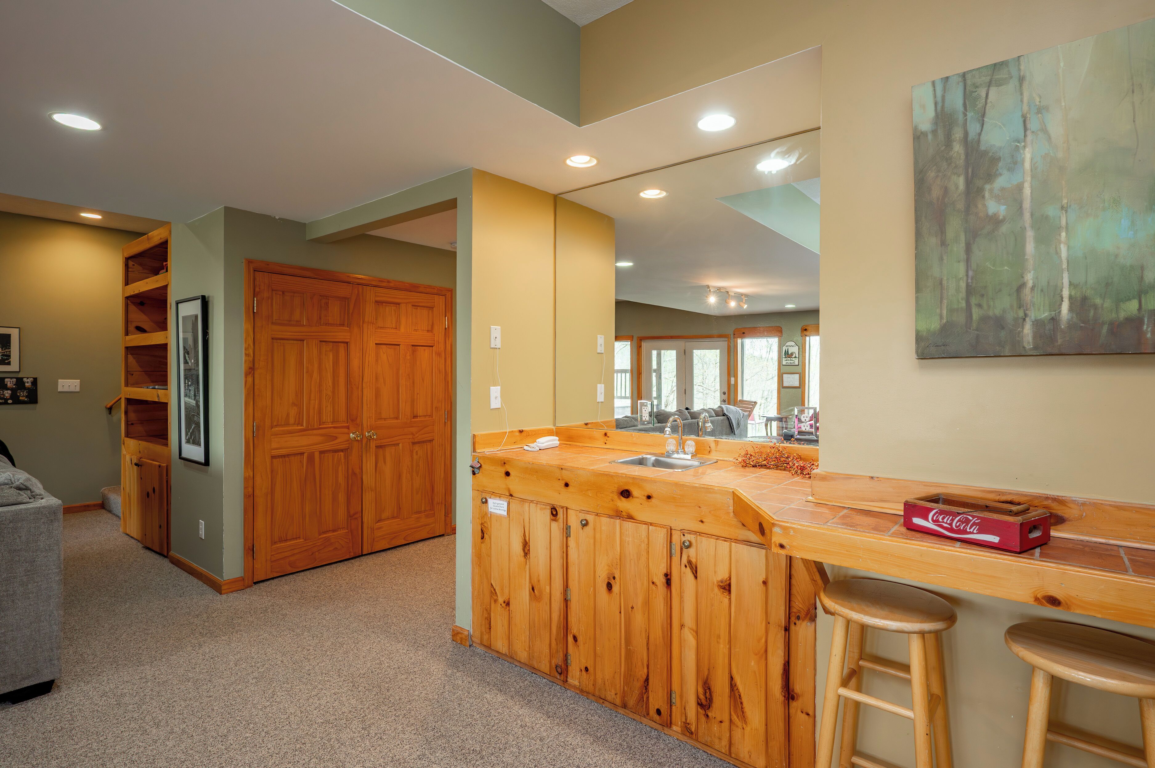 A kitchen with wooden cabinets, a bar area with stools, and a painting on the wall.