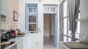 A modern kitchen with a brick wall, a toaster, a kettle, and a window with blue shutters. - Athenian Cypress House (Athina)