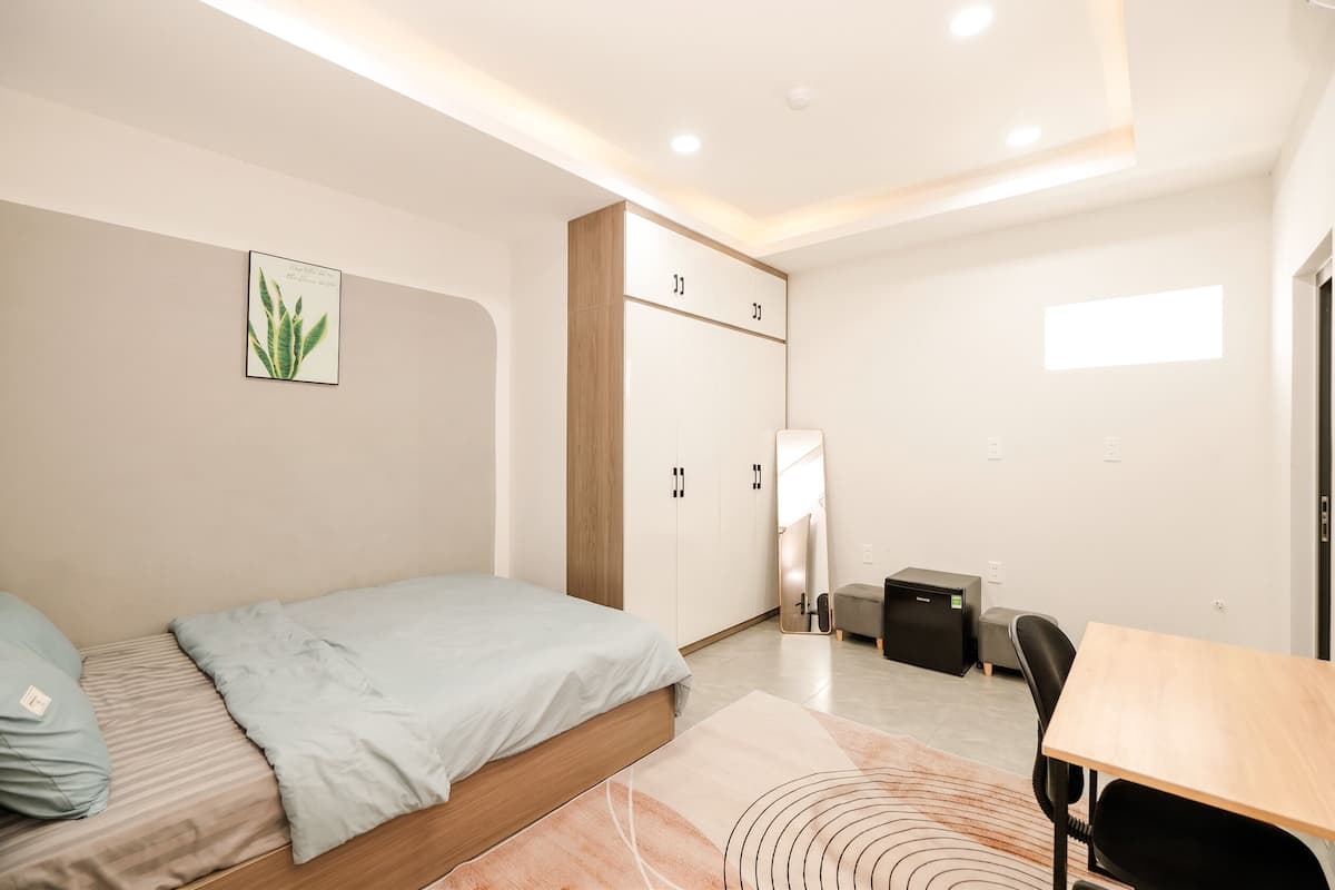 A modern bedroom with a bed, a desk, a wardrobe, and a small table.