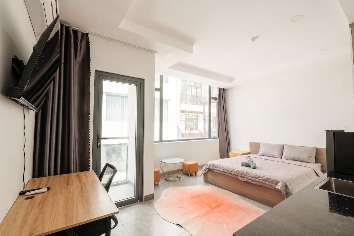 A modern bedroom with a bed, a desk, a chair, a small round table, and a large window.
