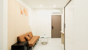 Een moderne hotelkamer met een bruine bank, een klein rond tafeltje en een deur naar een andere kamer.