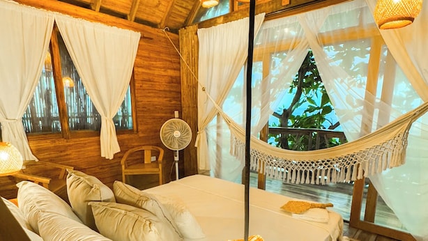 A cozy bedroom with a wooden ceiling, a hammock, and a bed with white linens. - Casa Dos Almas (Santa Marta)