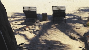 A beach with two black metal chairs facing the ocean, under a tree with string lights. - Casa Dos Almas (Santa Marta)