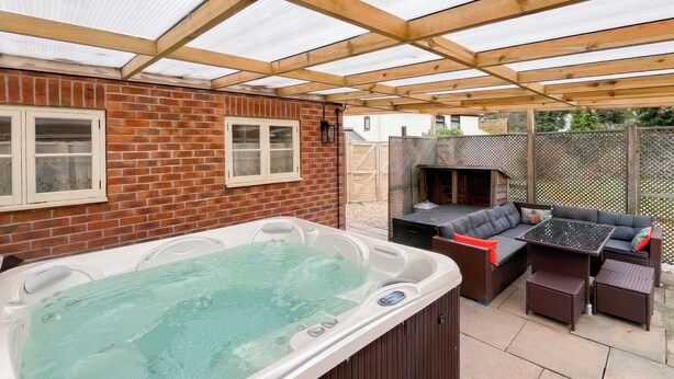 Ett bubbelbad och en utomhusplats med sittmöbler, ett pergola-tak, murade väggar och ett trädäck.