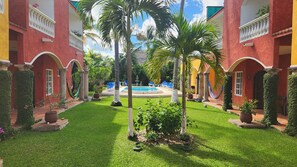 A courtyard with a pool, palm trees, and a red building with arches.