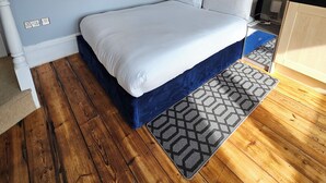 A bedroom with a bed, wooden flooring, a patterned rug, a mirror, and a dresser. - City centre location studio (Bristol)