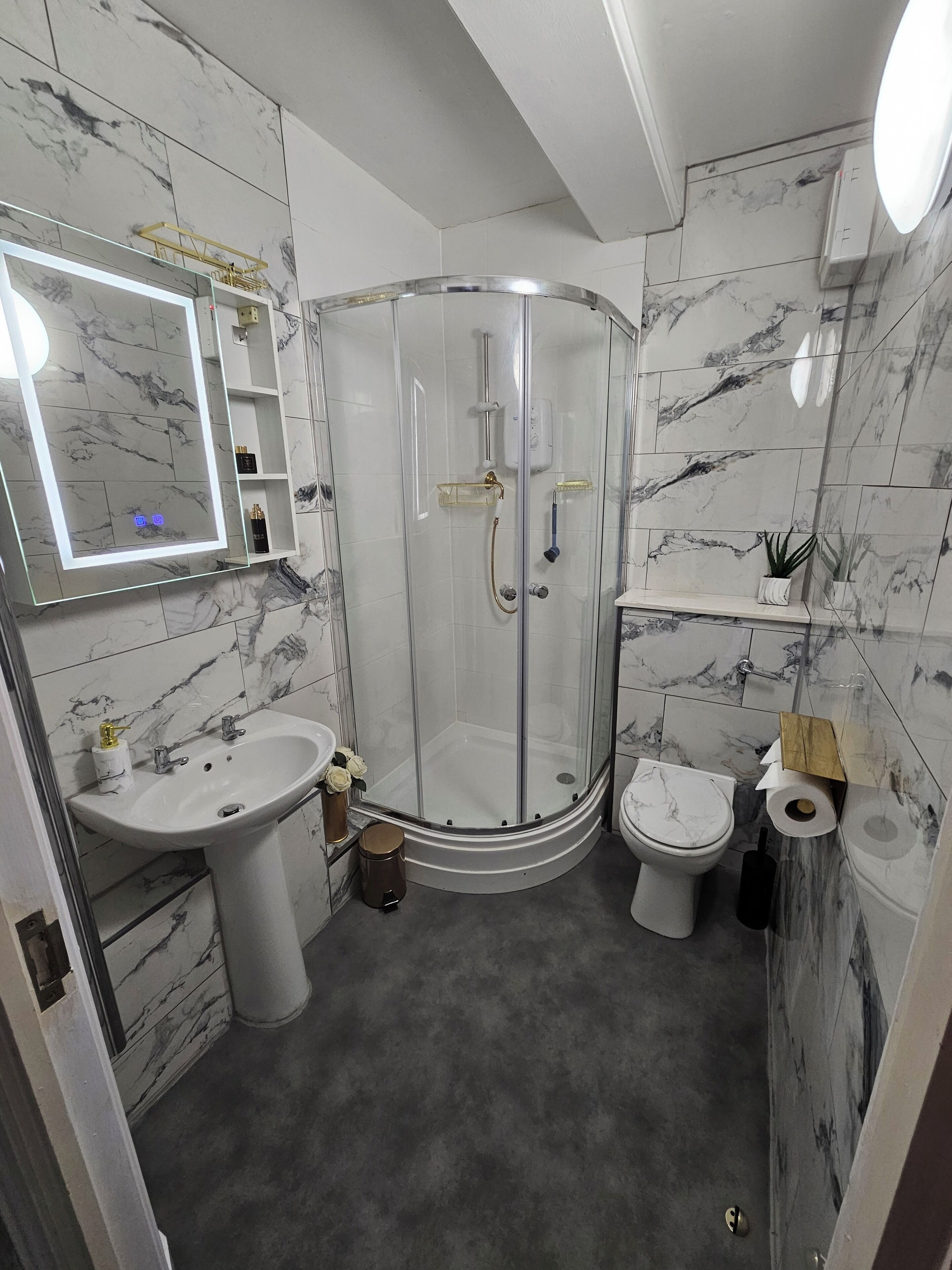 A modern bathroom with a glass-enclosed shower, a pedestal sink, and a toilet.