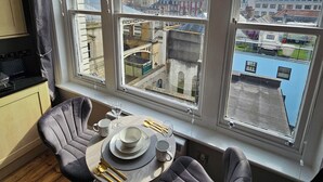 A dining area with a table set for two, two chairs, and a view of a cityscape through large windows. - City centre location studio (Bristol)