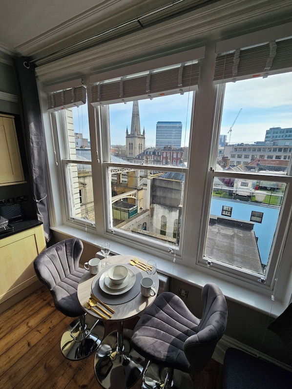 A dining area with a table set for two, two chairs, and a view of a cityscape through large windows.